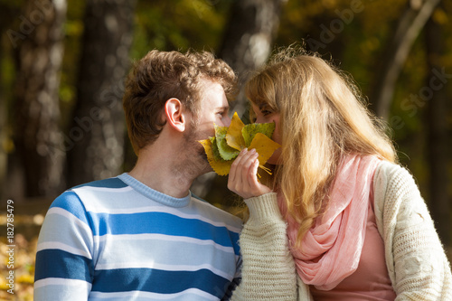 couple kissing in autumn park hiding behind leaves