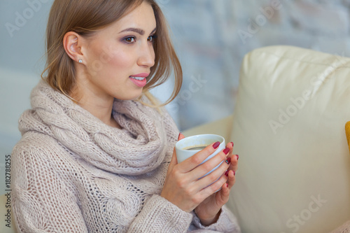 Beautiful woman holding a cup of coffee in her hands. in a knitted beige sweater