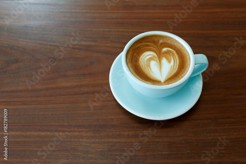 A cup of hot latte coffee with heart shape latte art on the wooden table