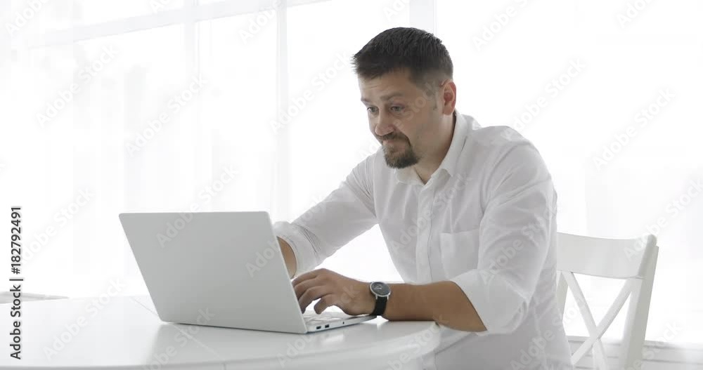 Stylish businessman in a white shirt nervously typing on a laptop and closing it. Stylish businessman in a white shirt nervously typing on a laptop and closing it.