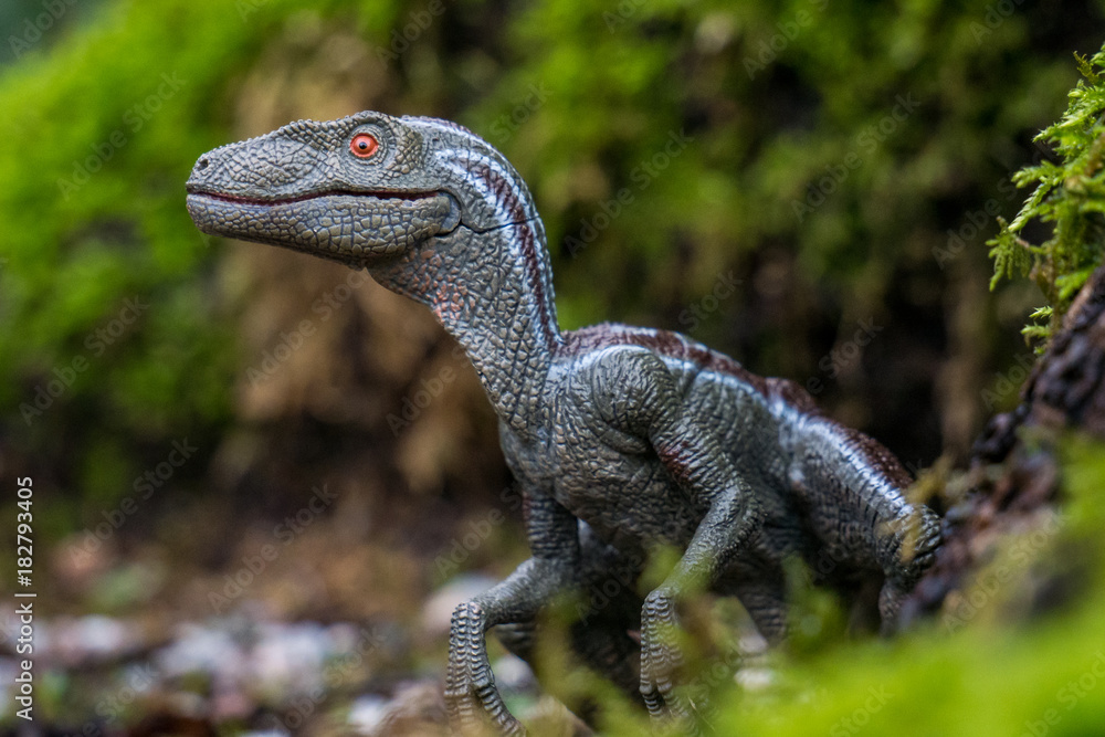 Fototapeta premium toy dinosaur raptor in the forest 