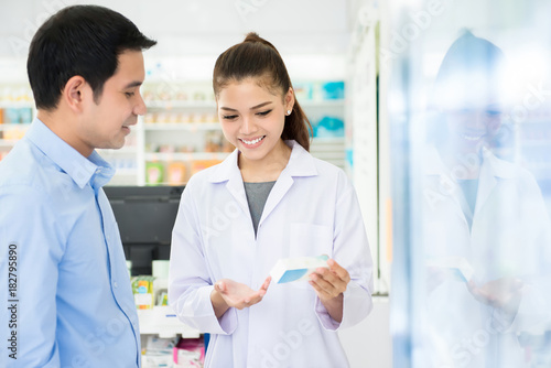 Female pharmacist holding medicine bottle giving advice to customer in pharmacy