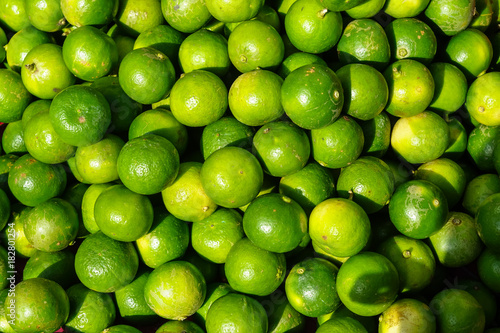 Pile of fresh rounded organic lime fruit background in bright yellow and green color selling in market under sunlight with light reflection skin