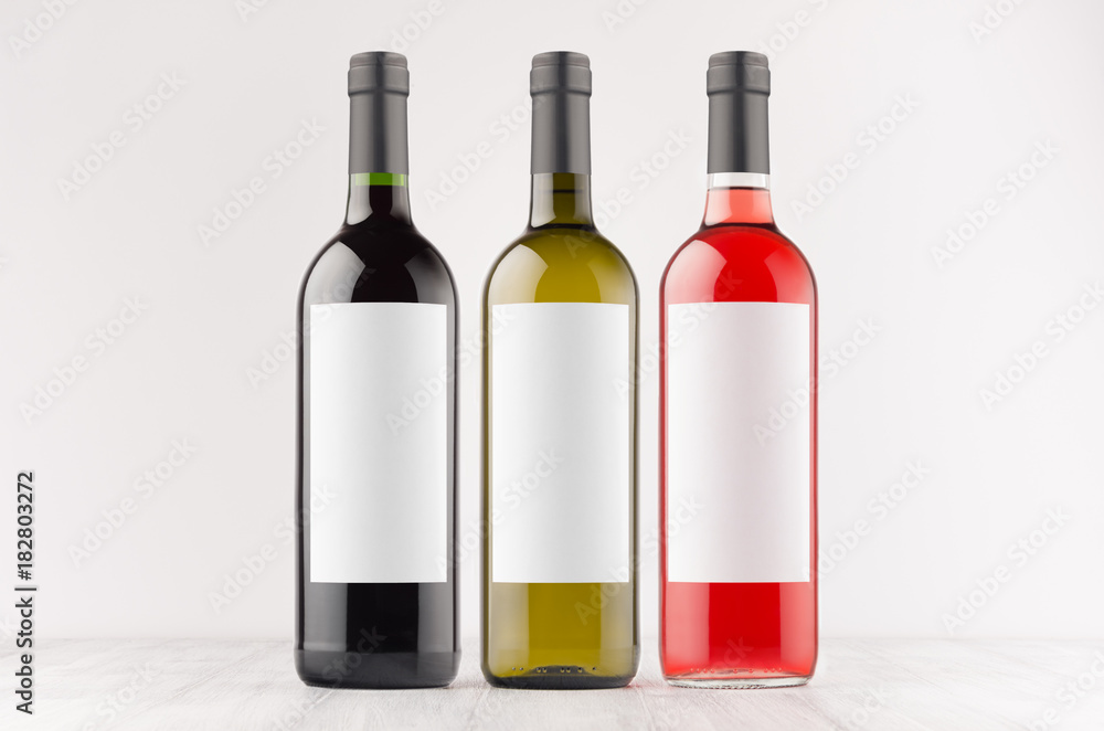 Three wine bottles - red, green, black - with blank white labels on white wooden board, mock up. Template for advertising, design, branding identity. Three wine bottles - red, green, black - with blank white labels on white wooden board, mock up. Template for advertising, design, branding identity.