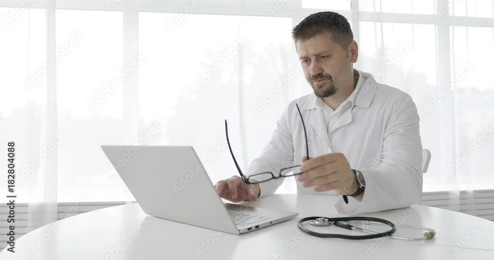 Tired man doctor works on a laptop in the clinic. Tired man doctor works on a laptop in the clinic.
