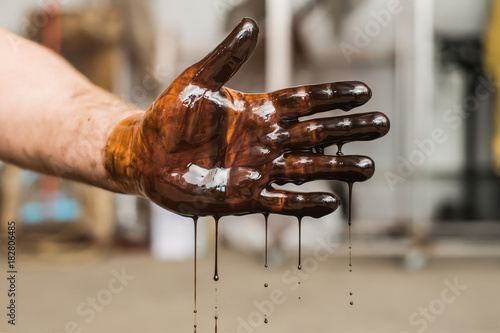 Used automotive oil completely covers the mechanic's arm and drips down