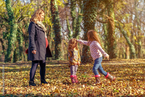 Pregnant mother enjoying with her two daughters in park on sunny autumn day.
