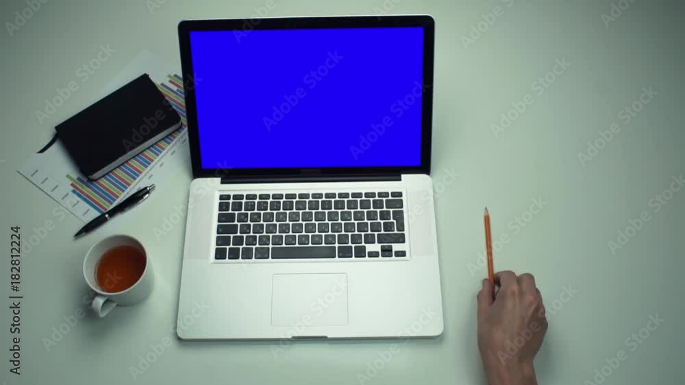Top view male hands working with printed graphs using laptop with green screen Top view male hands working with printed graphs using laptop with green screen