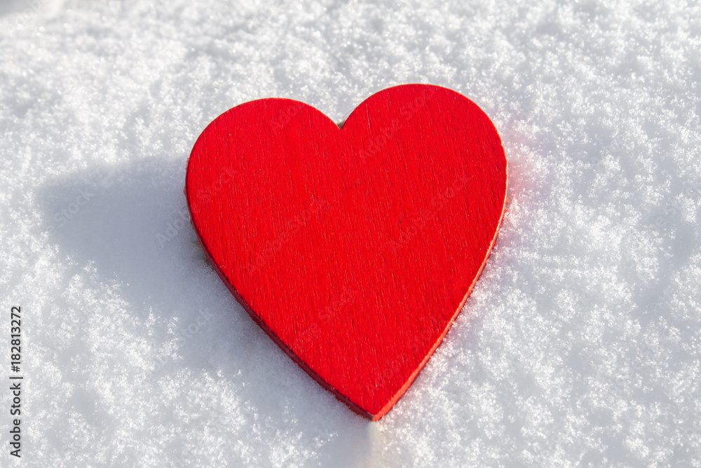 In the snow lies a red heart made of wood. Template for a holiday card with a white texture and free space for text. In the snow lies a red heart made of wood. Template for a holiday card with a white texture and free space for text.
