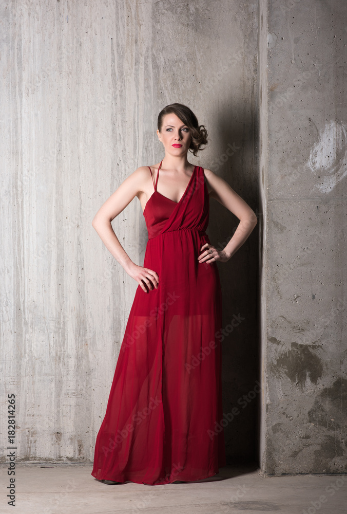 Vertical portrait of a beautiful young woman in long red dress in full growth on a background of gray concrete walls Vertical portrait of a beautiful young woman in long red dress in full growth on a background of gray concrete walls