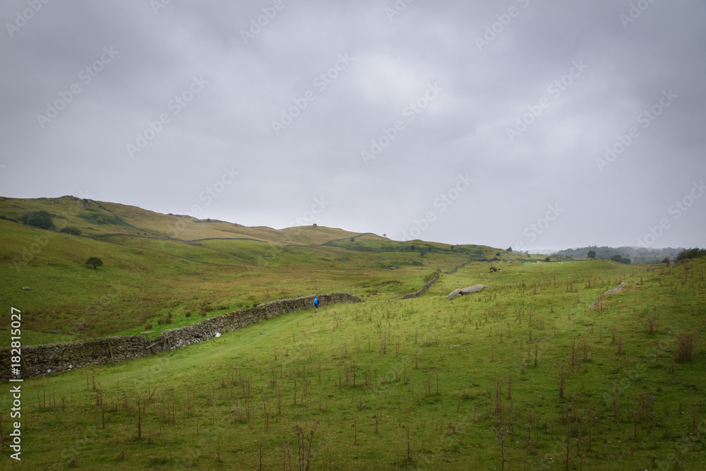 Hiker walking the Dales Way in the green and vast moorlands of England in moddy weather Hiker walking the Dales Way in the green and vast moorlands of England in moddy weather