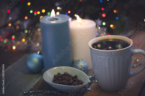 A romantic festive still life with burning candles and a bowl of coffee beans. A cup of freshly brewed coffee in a close up. Ligth blue colors. Dark Christmas background. Blurred bokeh