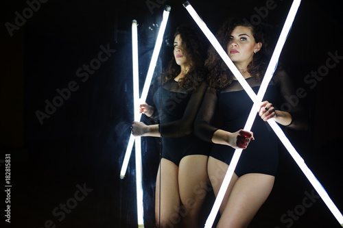 Curly brunette plus size model with two long led lamp at dance room with mirror. photo