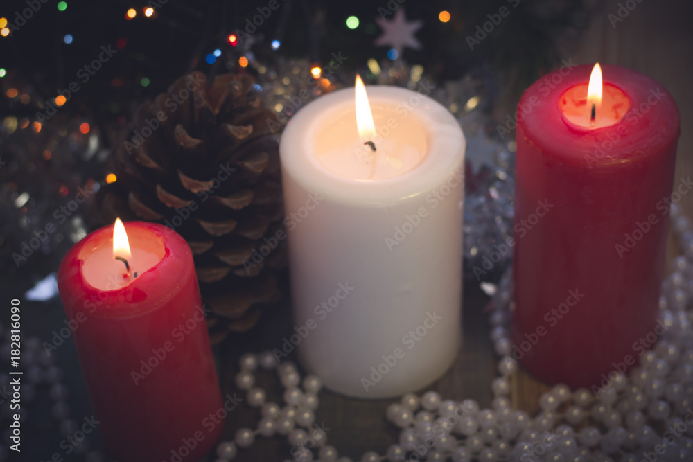 A romantic festive still life with burning candles, a pinecone and white pearl beads A colored wooden surface. White and red colors. Dark Christmas background. Blurred bokeh A romantic festive still life with burning candles, a pinecone and white pearl beads A colored wooden surface. White and red colors. Dark Christmas background. Blurred bokeh