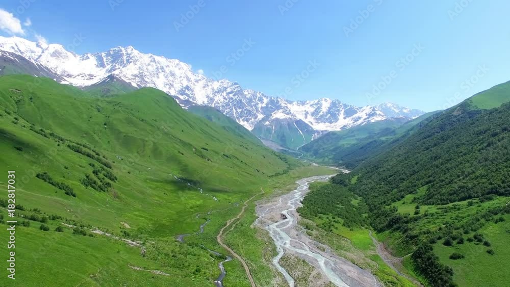 Aerial view of rocky mountain river in valley 4k nature video landscape background. Water flows, snow peak ridge on blue sky in Caucasus, Georgia