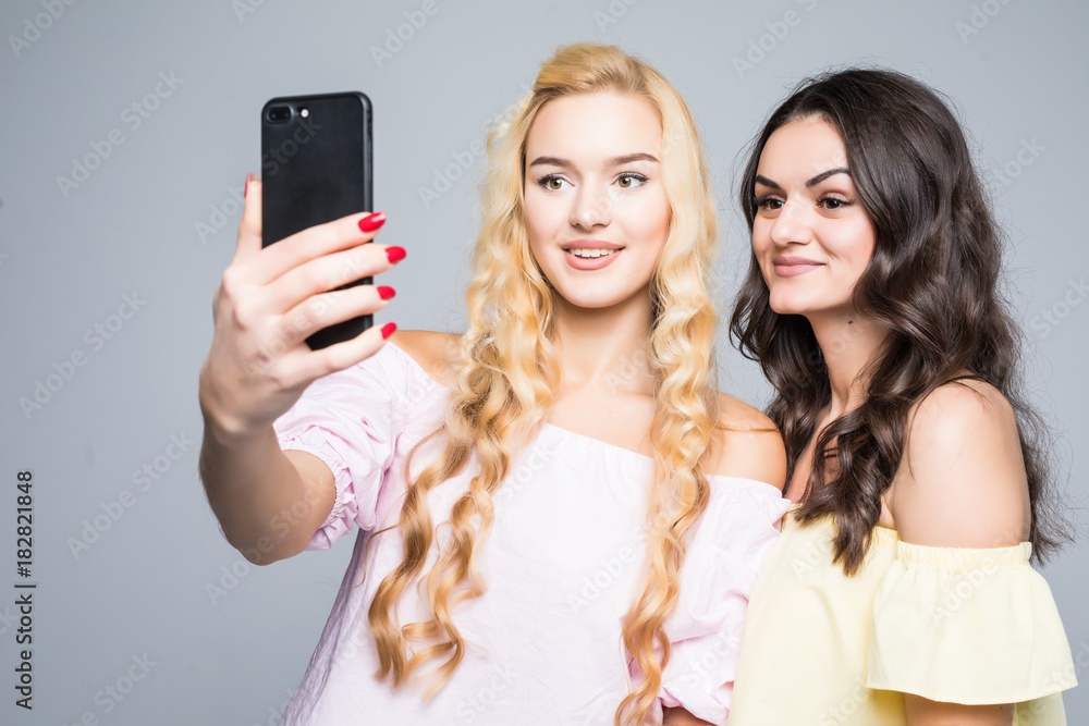 Portrait of a happy two smiling girls making selfie photo on smartphone on white background