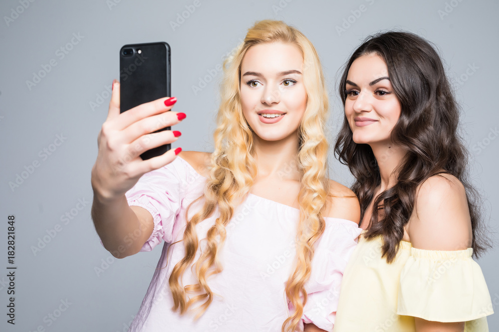 Portrait of a happy two smiling girls making selfie photo on smartphone on white background Portrait of a happy two smiling girls making selfie photo on smartphone on white background