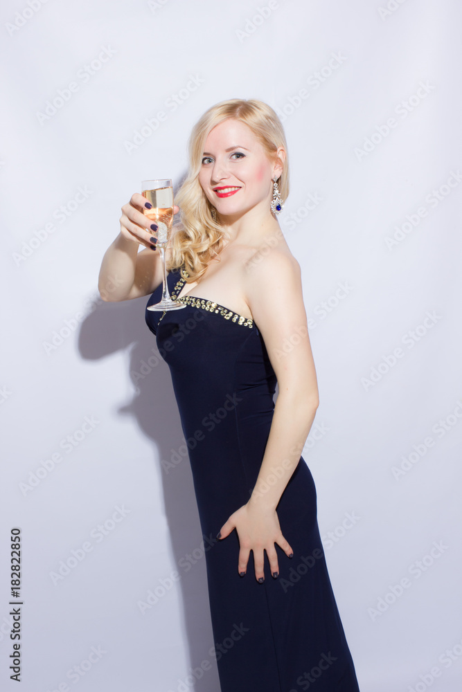 Studio portrait of a beautiful young blonde woman in a blue long evening dress. A girl is holding a glass of champagne in her hands Studio portrait of a beautiful young blonde woman in a blue long evening dress. A girl is holding a glass of champagne in her hands