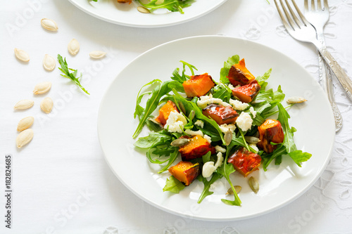 Fresh autumn salad with baked pumpkin, arugula, cheese and seeds on white table cloth. Space for copy