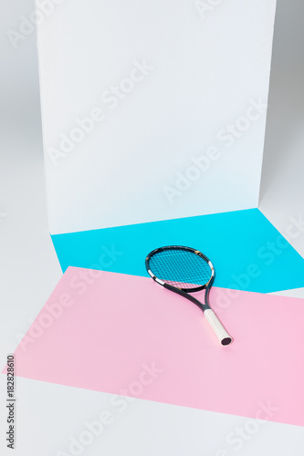 tennis racket lying on blue and pink papers at white wall