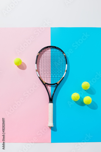 top view of tennis racket and yellow balls on blue and pink papers