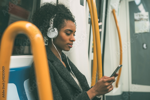 Happy young black woman sitting inside the underground listening to music