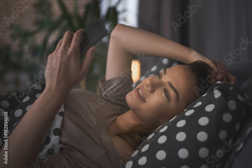 Girl lying down in bed at night and using smart phone for texting