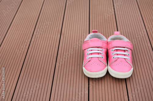 Pair of pink baby leather sneakers on wood plank background.