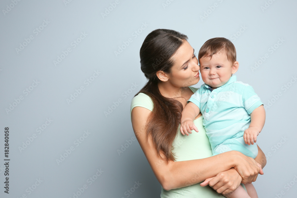 Young mother with little son on color background