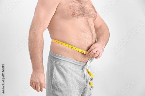 Overweight man with measuring tape on light background