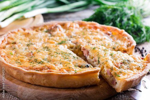 Sliced quiche with cheese and bacon on wooden background