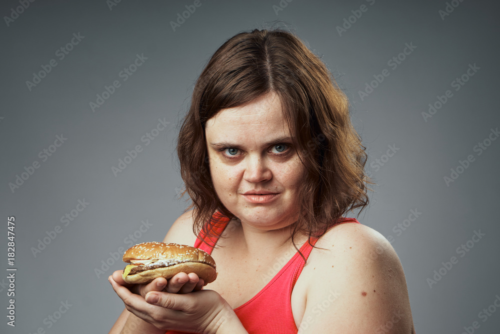 Fat woman holding a gray background hamburger, fast food Fat woman holding a gray background hamburger, fast food