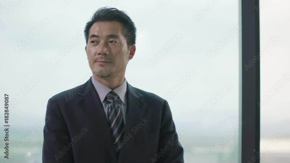 asian corporate executive looking around and thinking in front of window in office