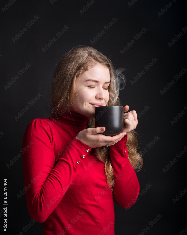 Beautiful young woman with cup of coffee, on black studio background. Smiling and cheerful woman holding a cup with hot tea. Winter girl drinking tea or coffee to warm up. Lifestyle studio photo. Beautiful young woman with cup of coffee, on black studio background. Smiling and cheerful woman holding a cup with hot tea. Winter girl drinking tea or coffee to warm up. Lifestyle studio photo.