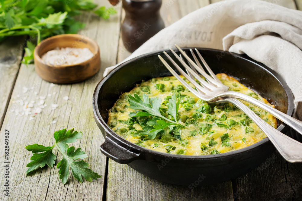 Fritatta with potatoes, green peas and herbs in an iron frying pan on an old wooden background. Selective focus. Rustic style. Fritatta with potatoes, green peas and herbs in an iron frying pan on an old wooden background. Selective focus. Rustic style.
