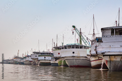 Traditional wooden sailing ships Bugis Pinisi line up in old port of Jakarta - Sunda Kelapa. View from Ciliwung river. Popular place to visit on Jakarta old town tour. Indonesia travel background. 