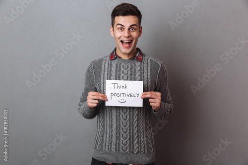 Happy screaming brunette man in sweater holding nameplate think positively
