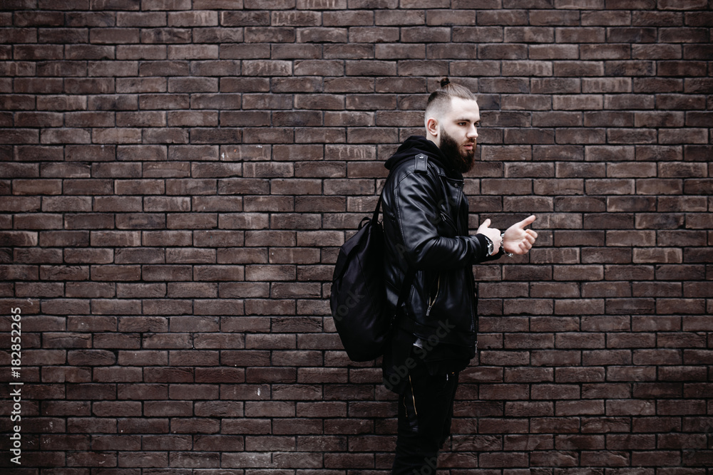 Modern young bearded man in black style clothes posing against brick wall. Modern young bearded man in black style clothes posing against brick wall.