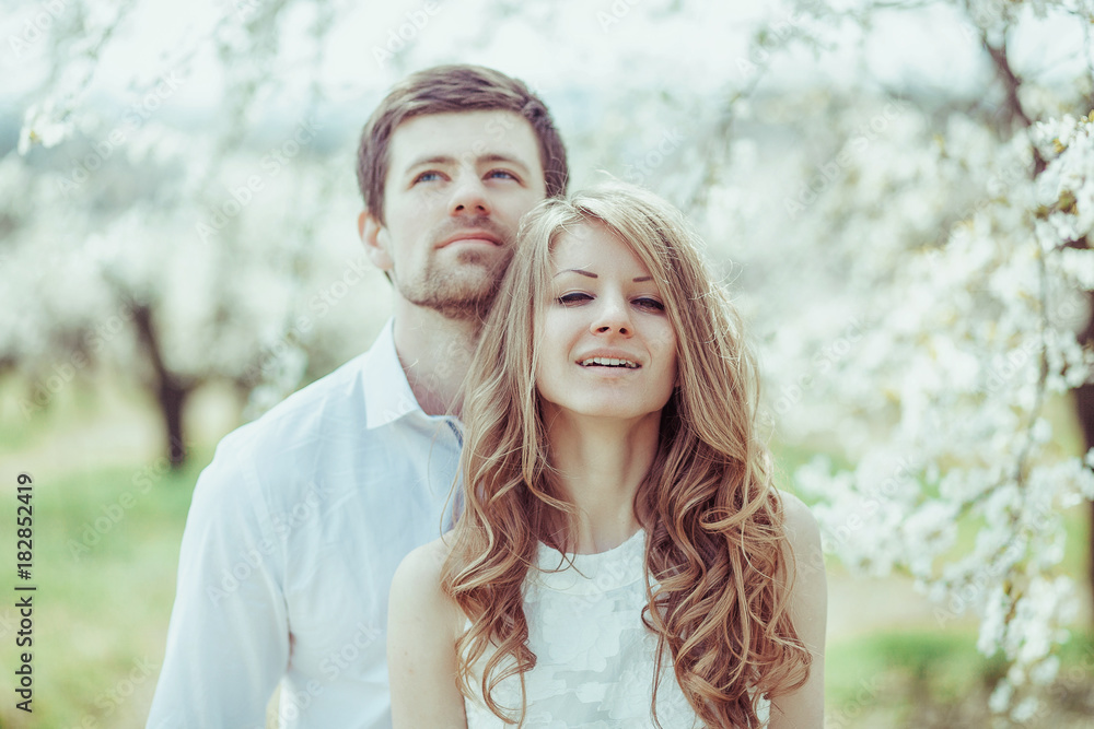 Fototapeta premium Happy Smiling Couple Relaxing in blooming apple tree garden. Man looking up. Portrait horizontal shot