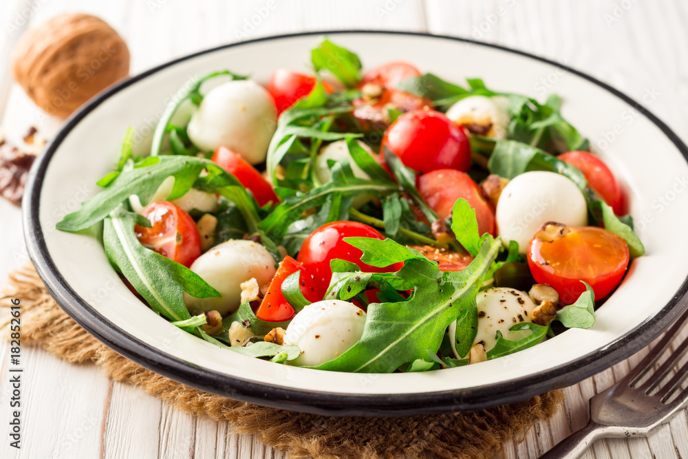 Fresh salad with arugula, cherry tomatoes, mozzarella cheese and walnuts on white wooden background. Fresh salad with arugula, cherry tomatoes, mozzarella cheese and walnuts on white wooden background.