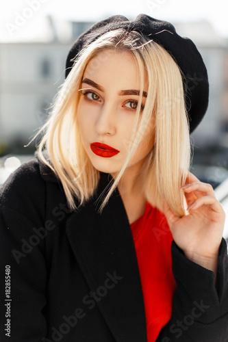 Vintage portrait of a beautiful young blonde woman with red lips in a black coat with a beret on an autumn sunny day photo