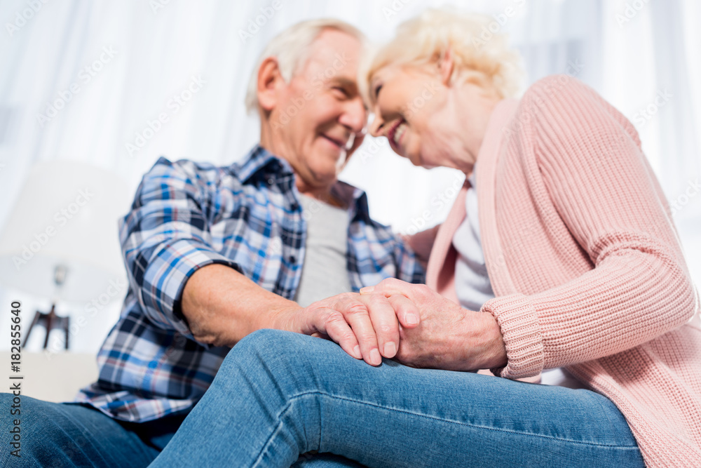 selective focus of happy senior couple looking at each other and holding hands selective focus of happy senior couple looking at each other and holding hands