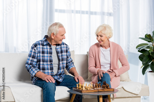 senior couple playing chess at home while sitting on couch