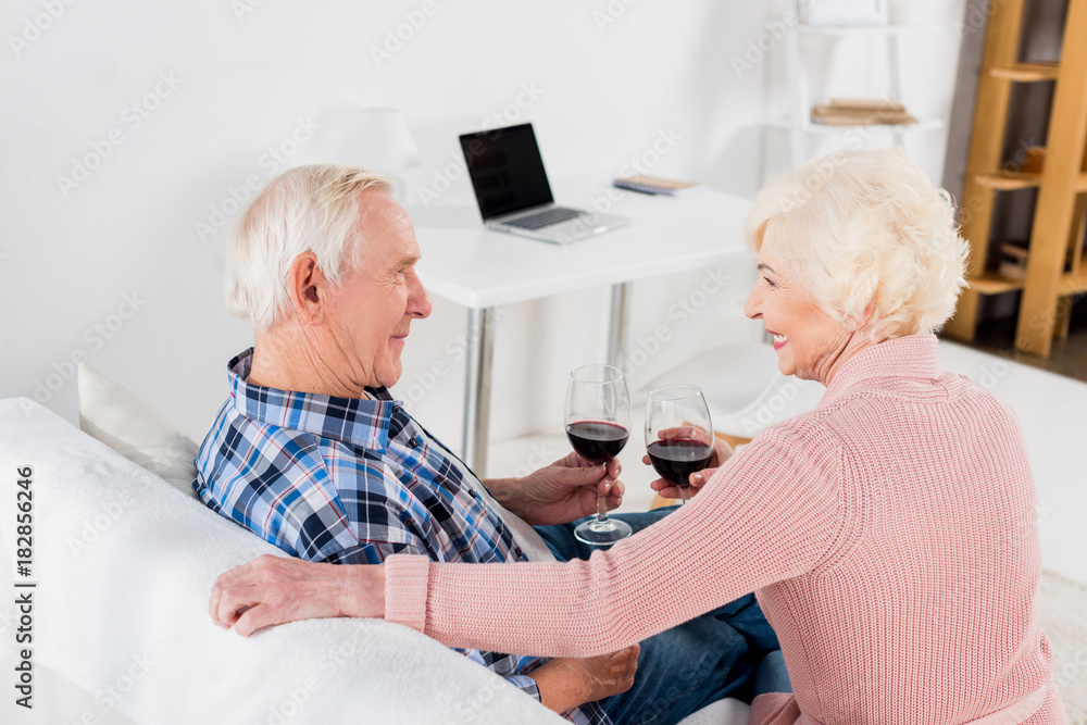 back view of senior man and woman with glasses of red wine looking at each other at home back view of senior man and woman with glasses of red wine looking at each other at home