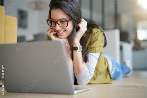 Brunette woman laying on floor, connected on internet with laptop