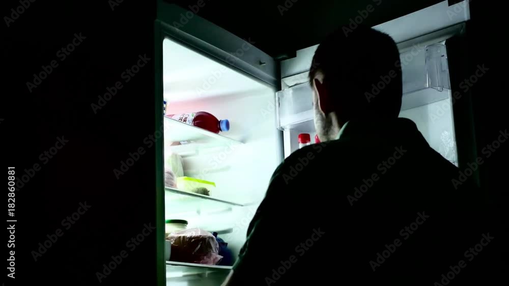 A man standing in the kitchen at night opens the refrigerator, drinks milk, a hungry guy. A man standing in the kitchen at night opens the refrigerator, drinks milk, a hungry guy.