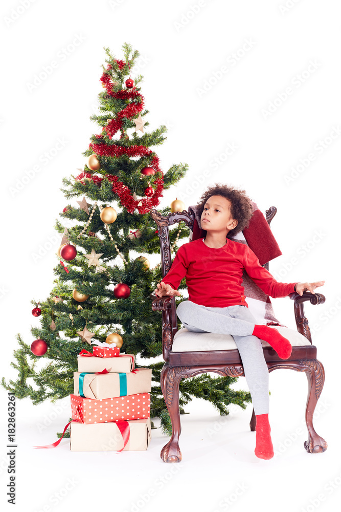 Portrait of cute mixed race little boy sitting in chair near Christmas tree Portrait of cute mixed race little boy sitting in chair near Christmas tree