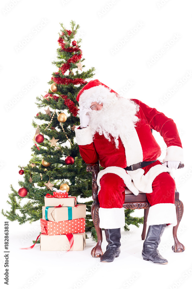 Portrait of Santa Claus sleeping in chair next to Christmas tree, heap of gift boxes near him