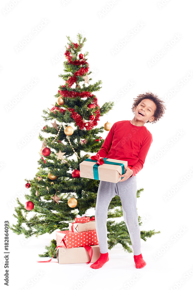Portrait of cute mixed race little boy standing near Christmas tree with gift box in his hands Portrait of cute mixed race little boy standing near Christmas tree with gift box in his hands
