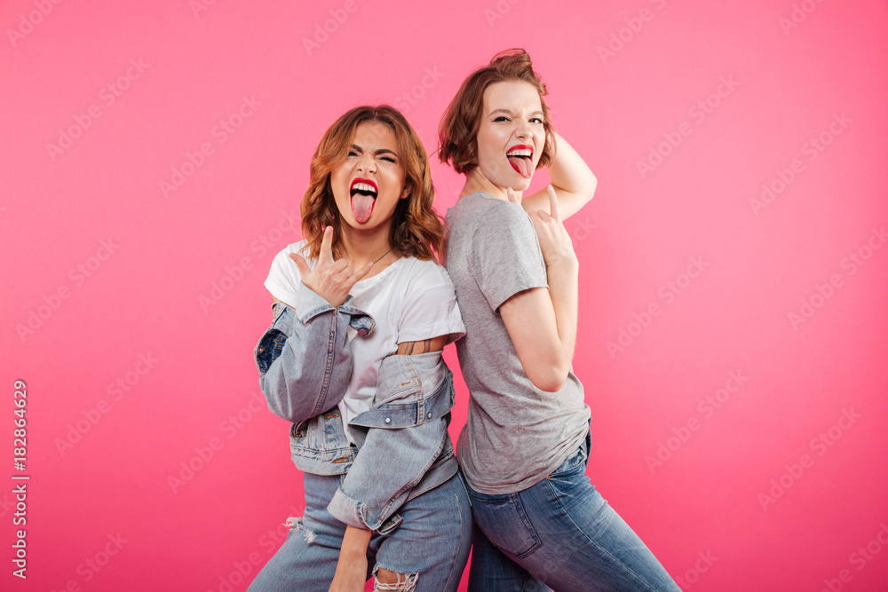 Ladies friends standing isolated showing rock gesture and tongue. Ladies friends standing isolated showing rock gesture and tongue.